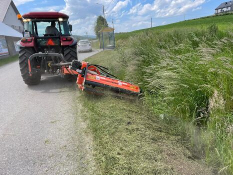 Traktor z przypiętym urządzeniem kosi trawę na poboczu drogi